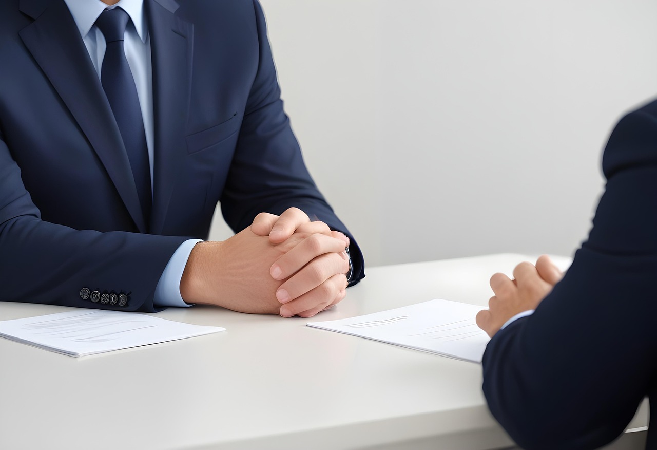 Deux personnes en entretien d’embauche, assises face à face à une table, sans que leurs visages ne soient visibles.